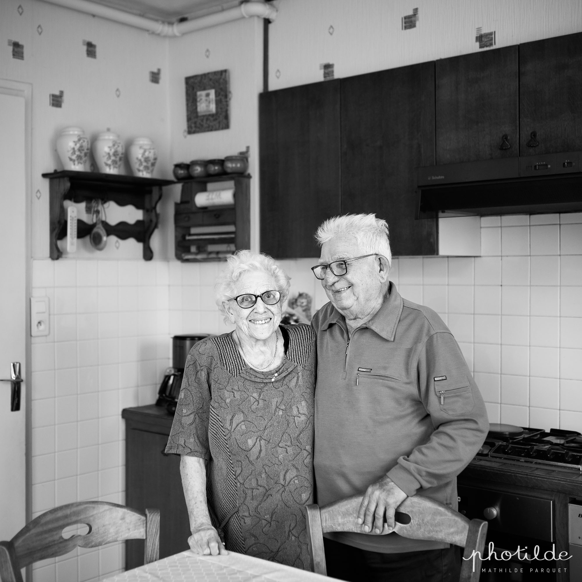 Couple de nonagénaire souriant debout dans leur cuisine.